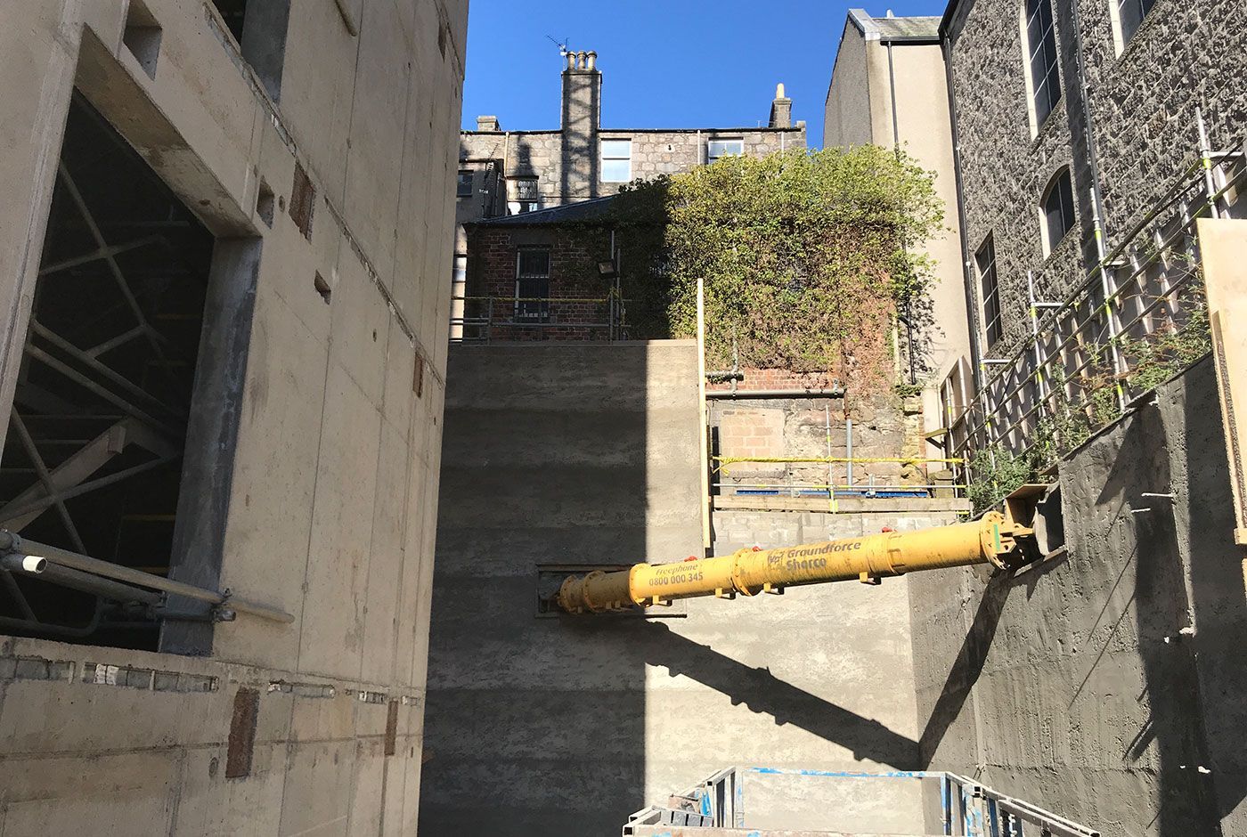 Construction site in an urban area with concrete walls and a yellow pipe spanning the space.
