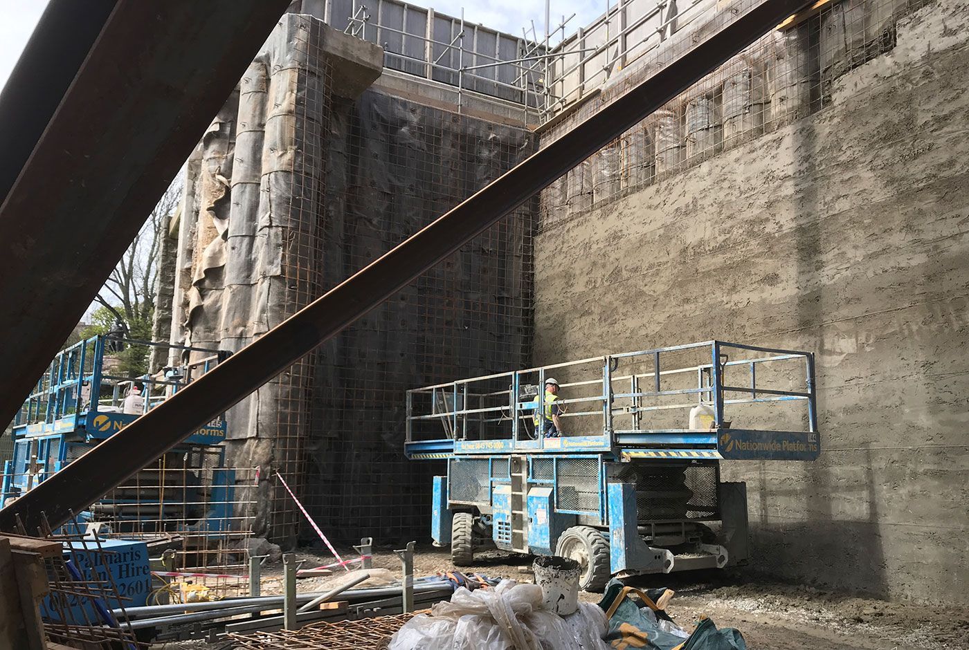 Blue scissors lift ready for use and parked next to contiguous piled walls.