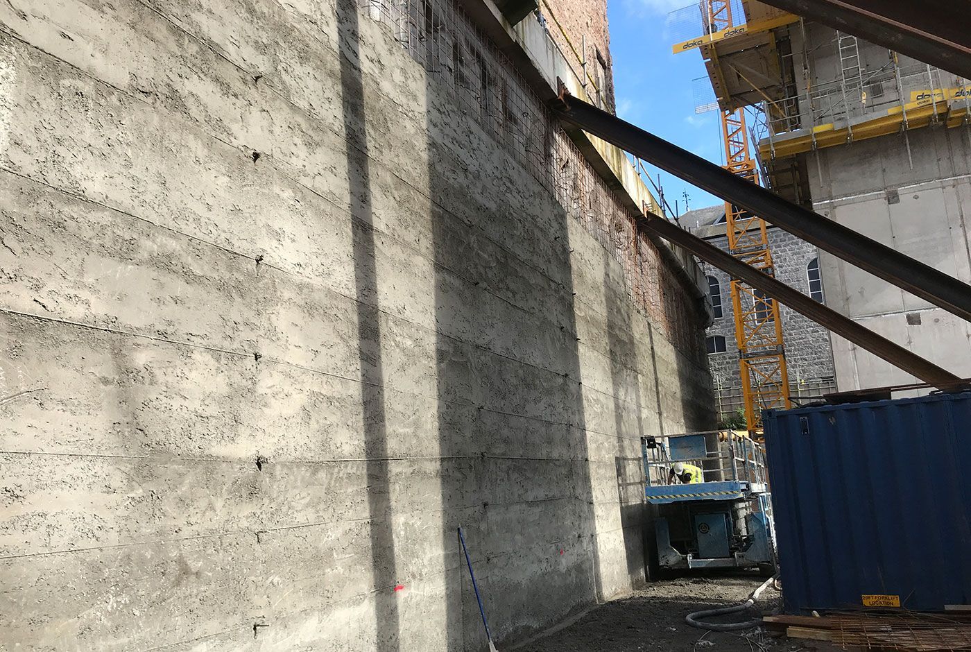 Construction site with a concrete wall, blue container, and scissor lift in the background.