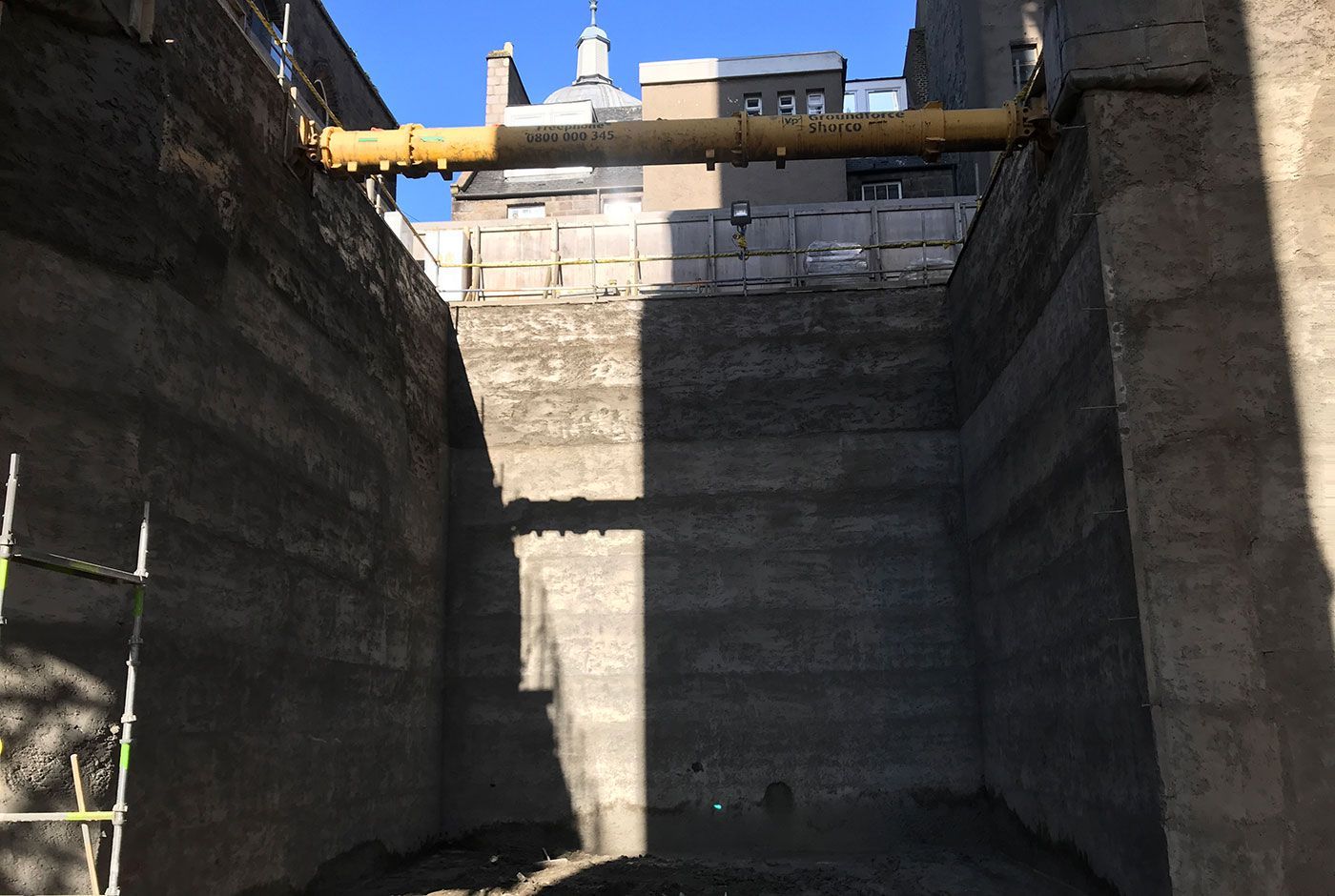 Concrete space with tall walls, sunlight above, and a yellow metal beam spanning two sides.