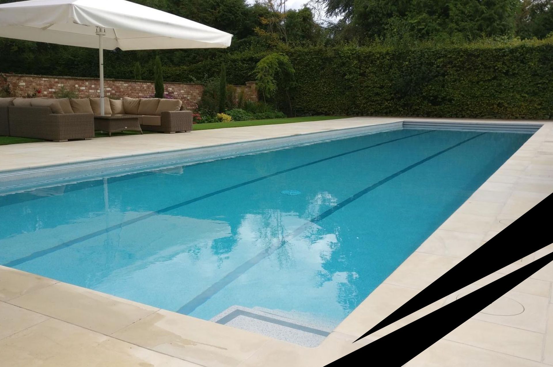 Outdoor swimming pool with clear blue water, large white umbrella and seating, surrounded by wall and greenery.