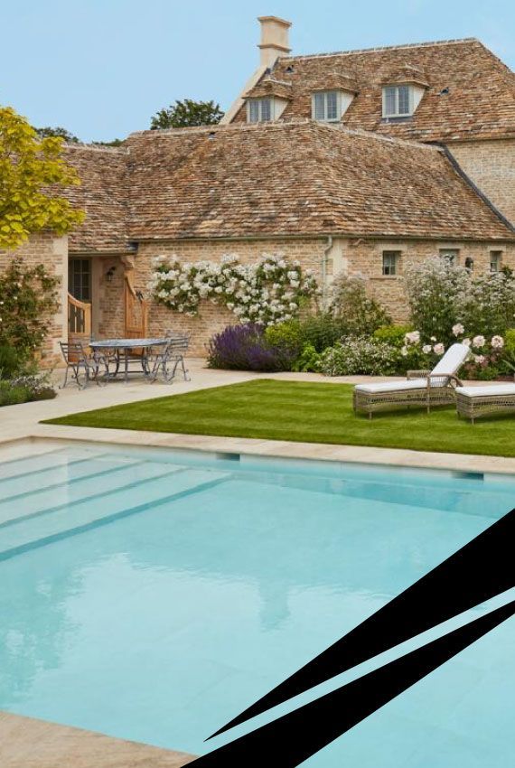 Stone cottage with a tiled roof, garden and swimming pool in the foreground.