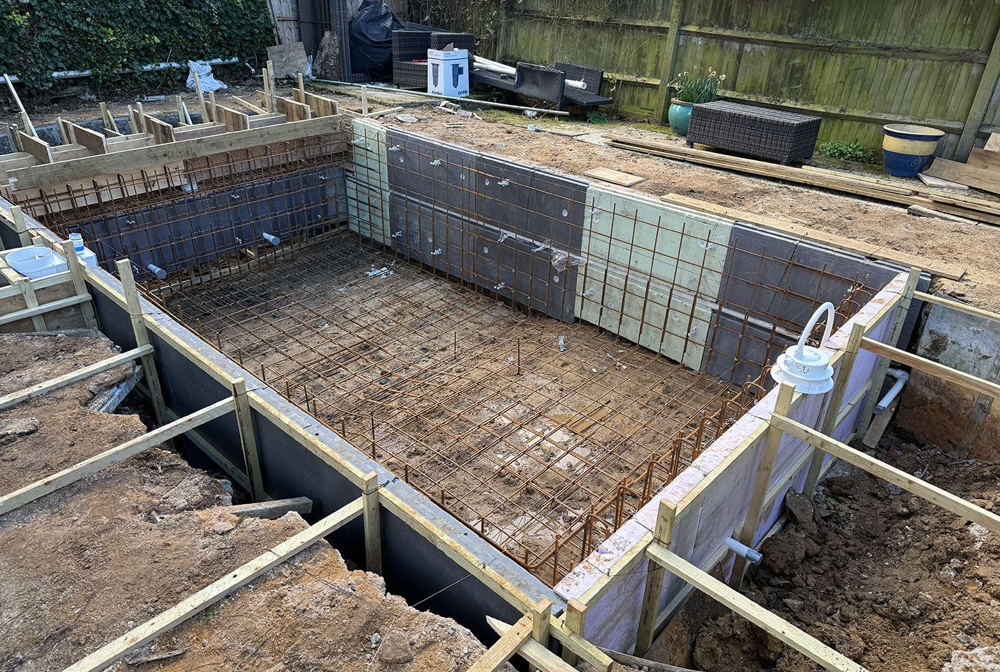 Rectangular framework for a swimming pool with rebar, wooden braces, and soil around the perimeter