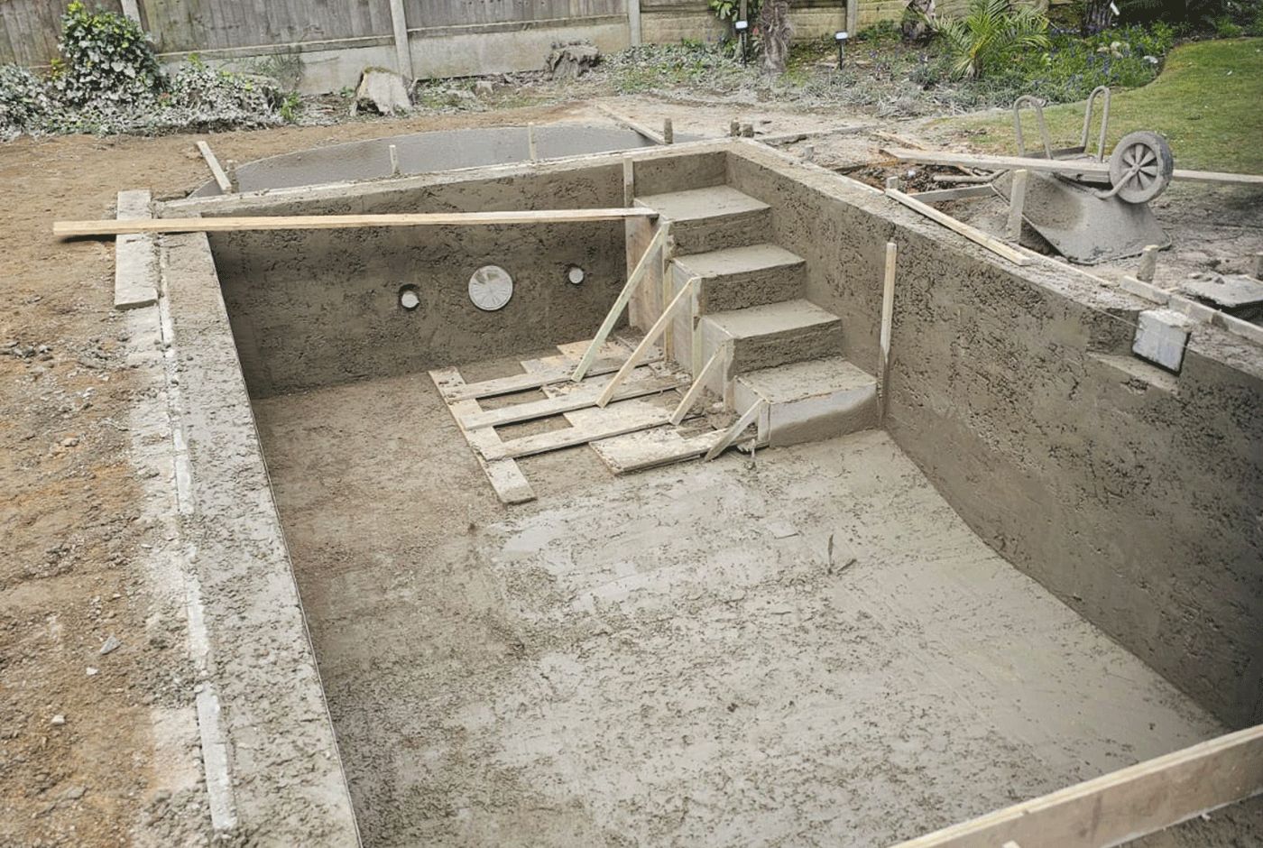 Rectangular concrete swimming pool shell under construction with formed steps and freshly sprayed floor.