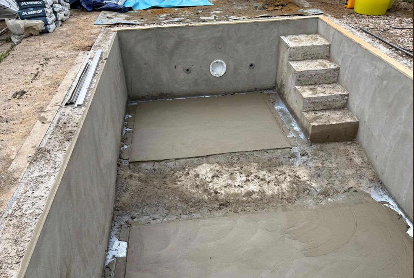 Concrete swimming pool under construction with built-in steps and two slabs of concrete in the base.
