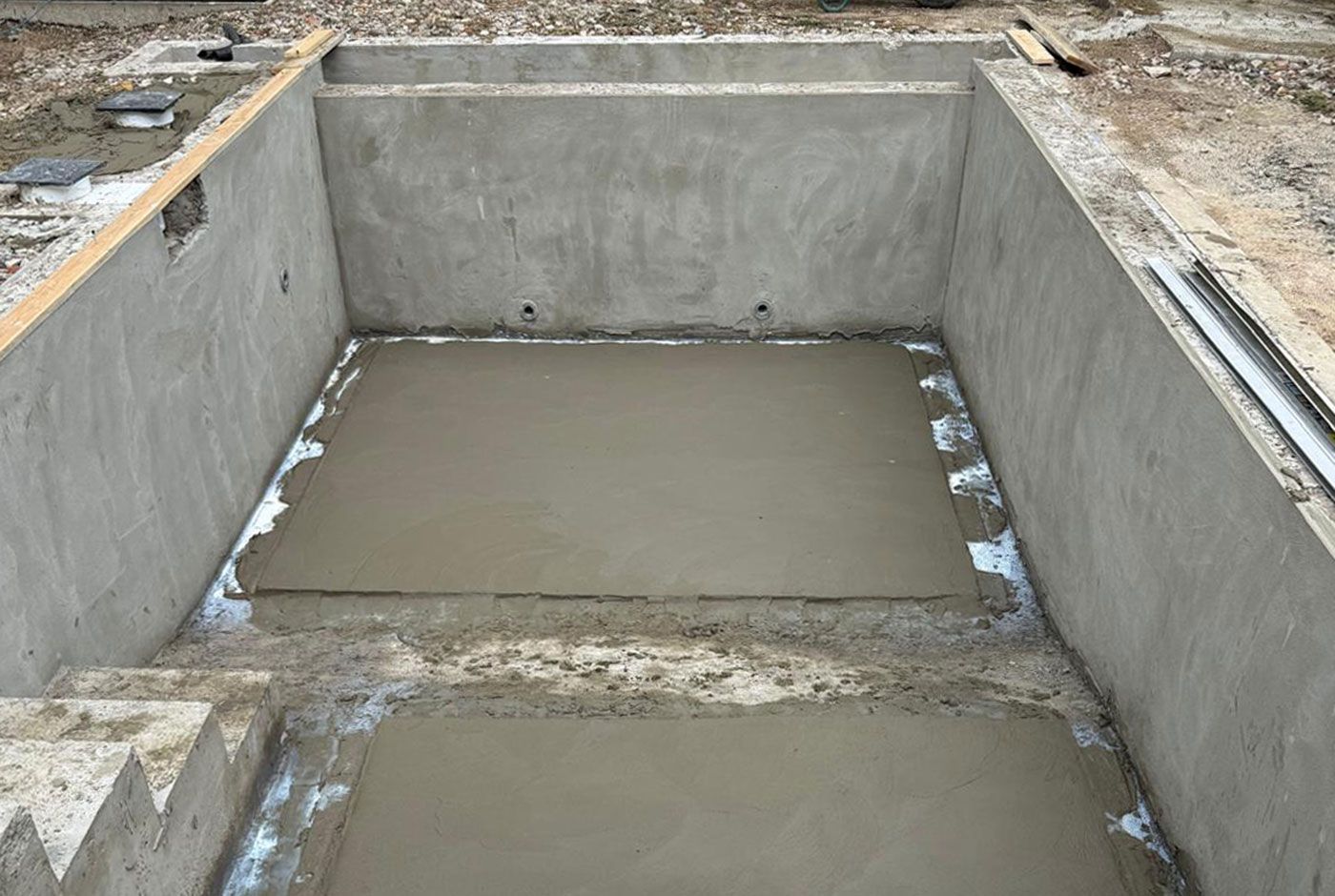 One end of a rectangular swimming pool shell, with concrete walls, steps down and freshly laid concrete base.