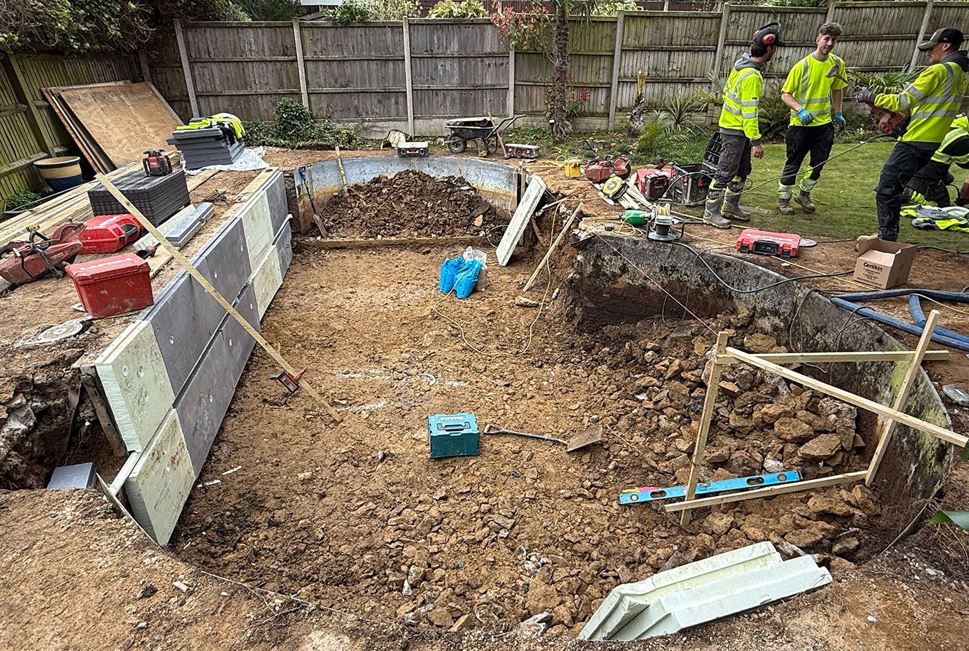 Excavation of an old residential swimming pool with workers in hi-viz and tools and equipment around the site.