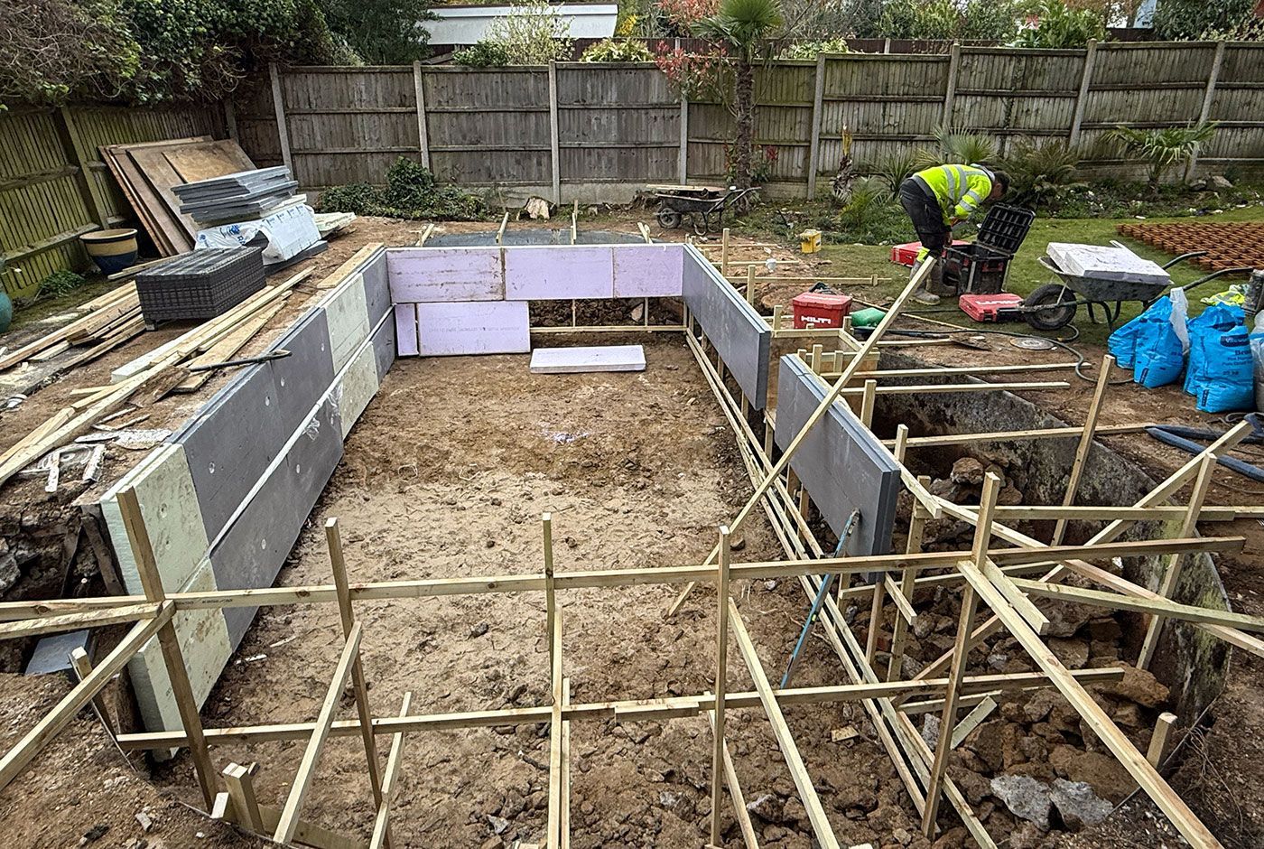 The wooden framework of a rectangular pool being installed in a garden, with tools scattered around.