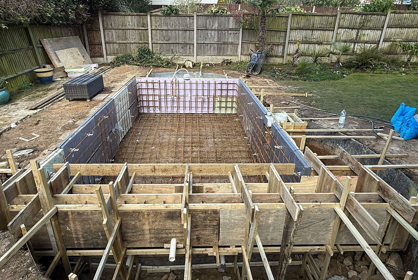 Construction site of a swimming pool with timber formwork and steel rebar for concreting in a garden.