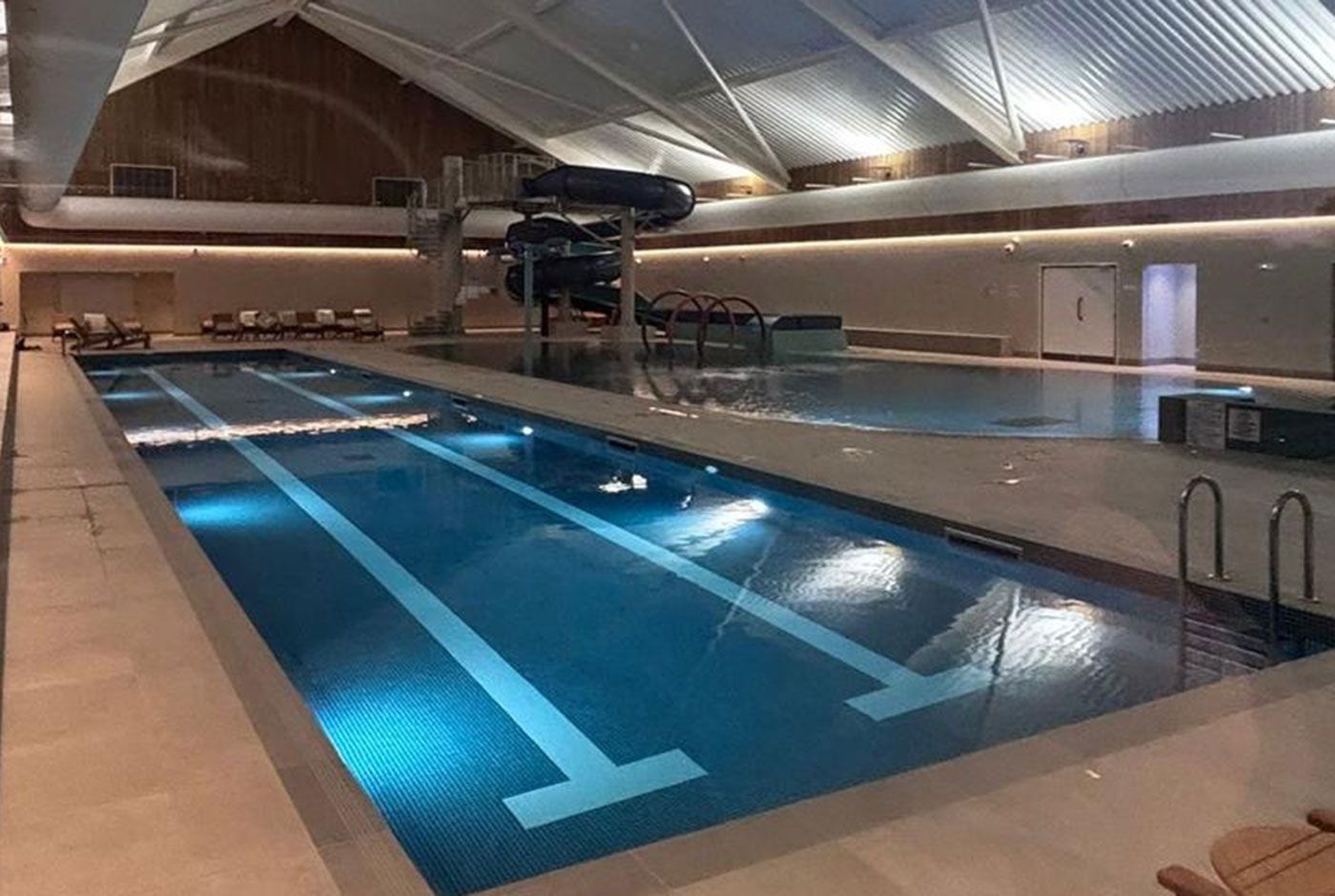 Luxury indoor swimming pool with lanes, blue water, and a pitched ceiling under bright lights.