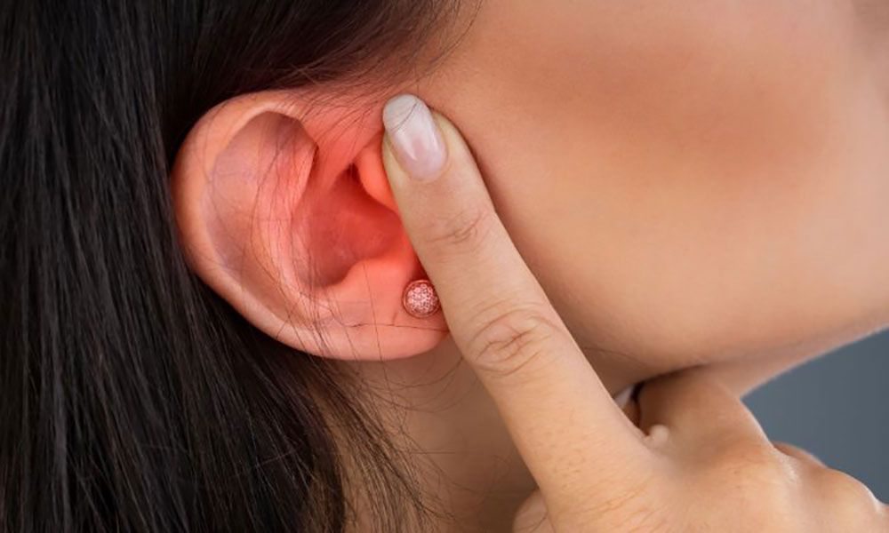 Hand pressing on a red ear, showing ear pain or discomfort