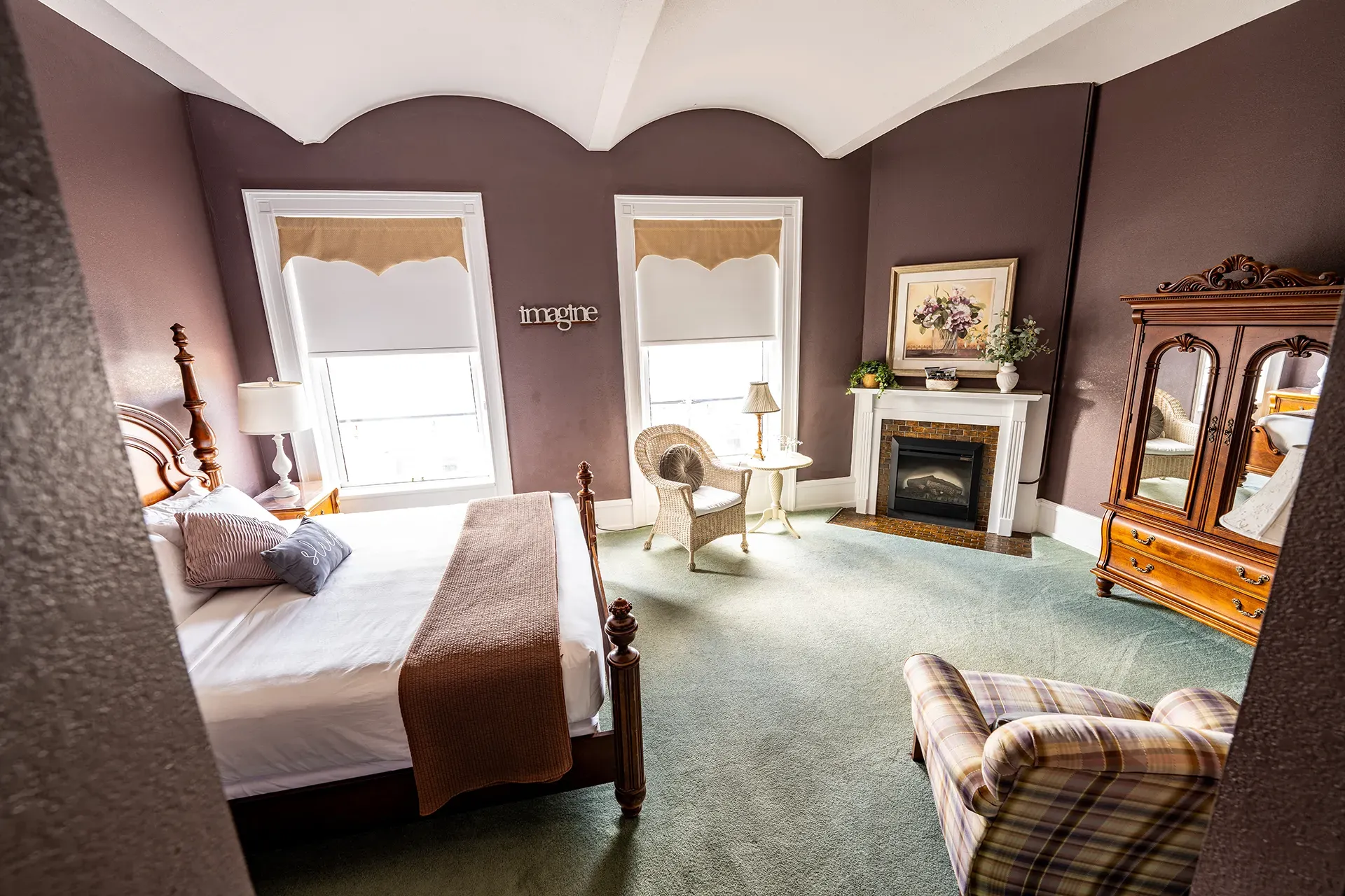 A bedroom with a bed , chair , fireplace and dresser.