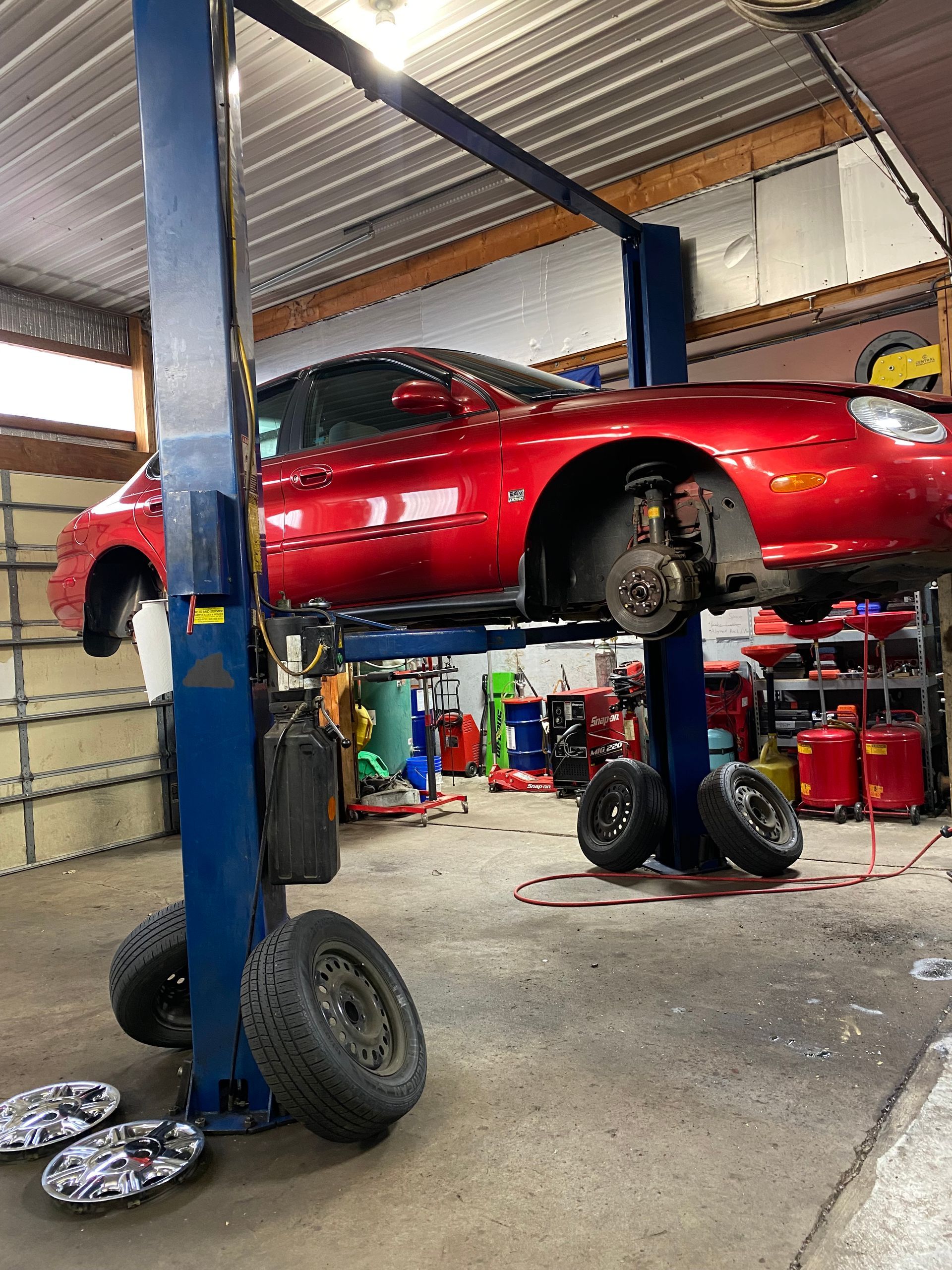Red sports car raised on a lift in an auto repair shop, with its front wheel removed. | Herstine Automotive LLC