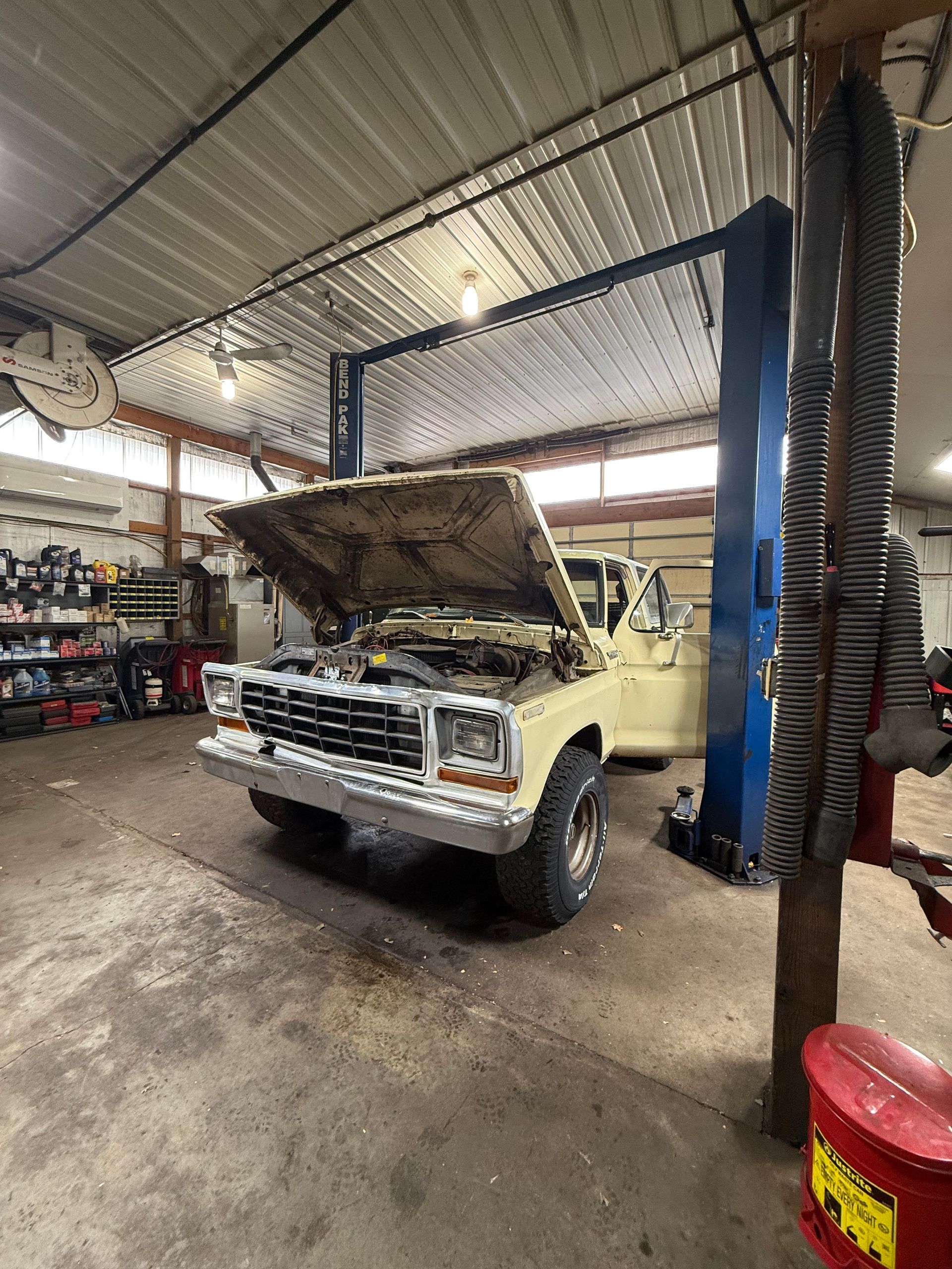 Yellow classic car in a garage with its hood open, showing the engine bay. | Herstine Automotive LLC