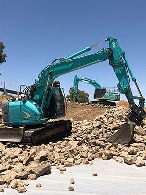A couple of excavators are sitting on top of a pile of rocks.