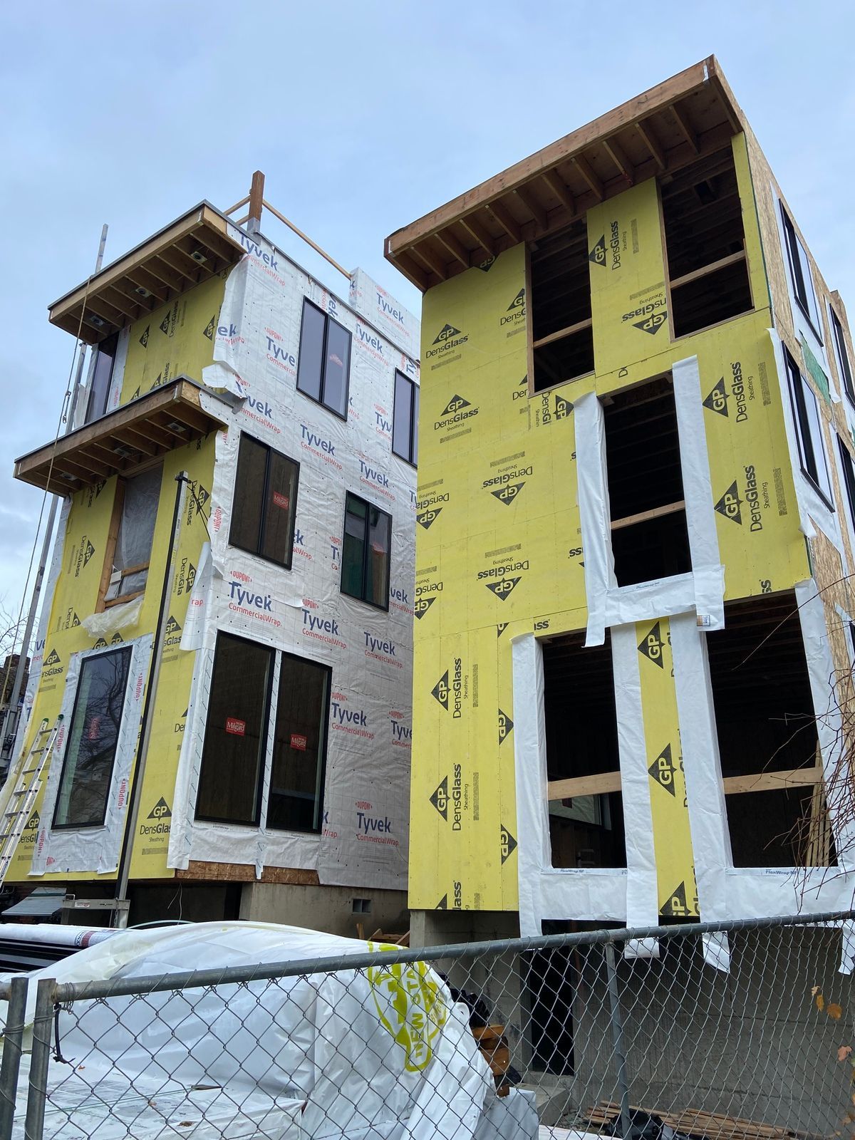 A building under construction with yellow insulation and a chain link fence surrounding it.