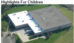 Overhead view of a Highlights for Children building with a white and gray roof, surrounded by green grass.