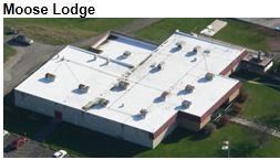 Aerial view of a Moose Lodge building with a white roof, several vents, and surrounded by grass and parking areas.