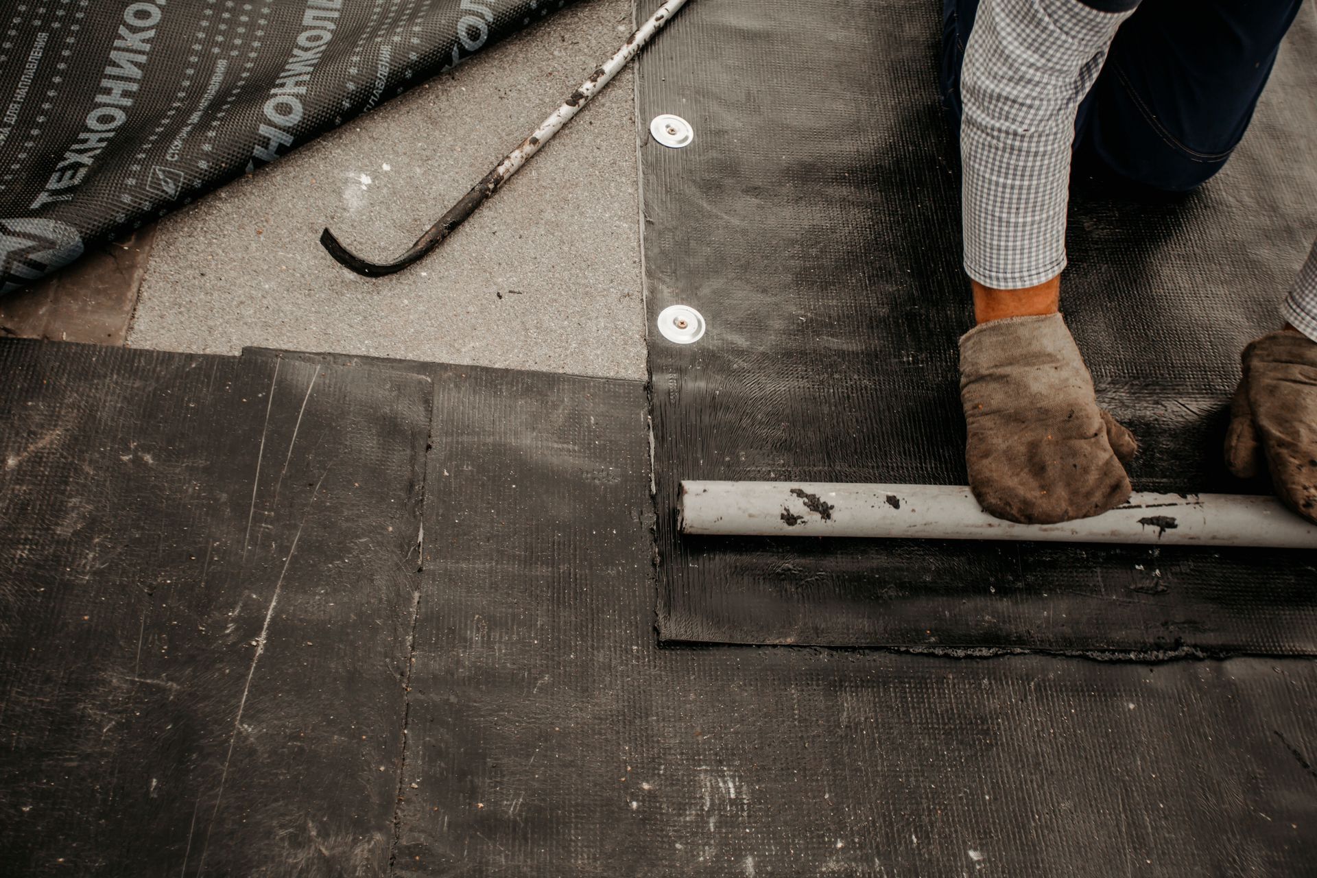 Close-up of a roofer installing a waterproof membrane during commercial flat roof construction.