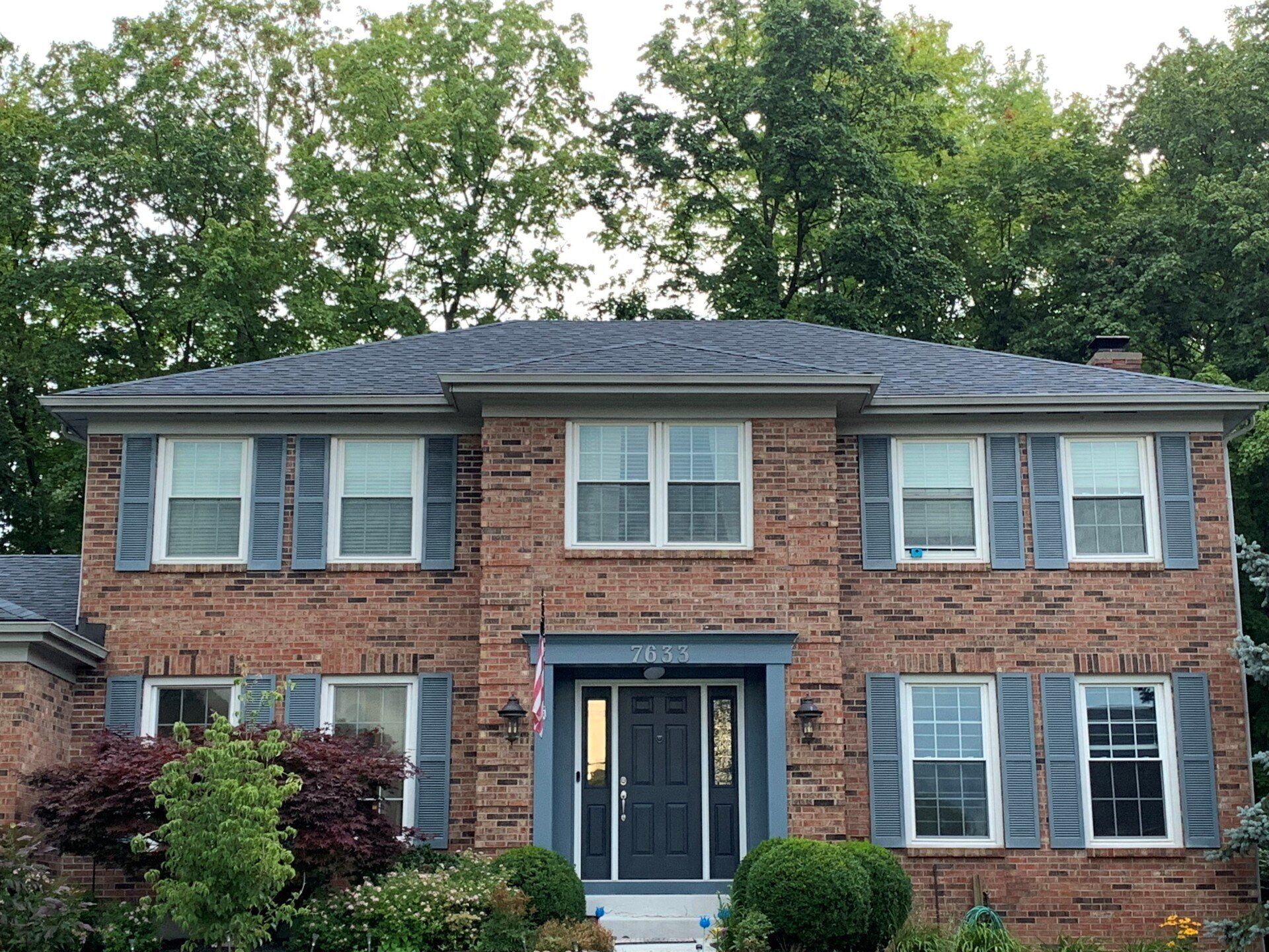Two-story brick house with gray roof, windows, and shutters. Front door is dark gray. Landscaping in front.