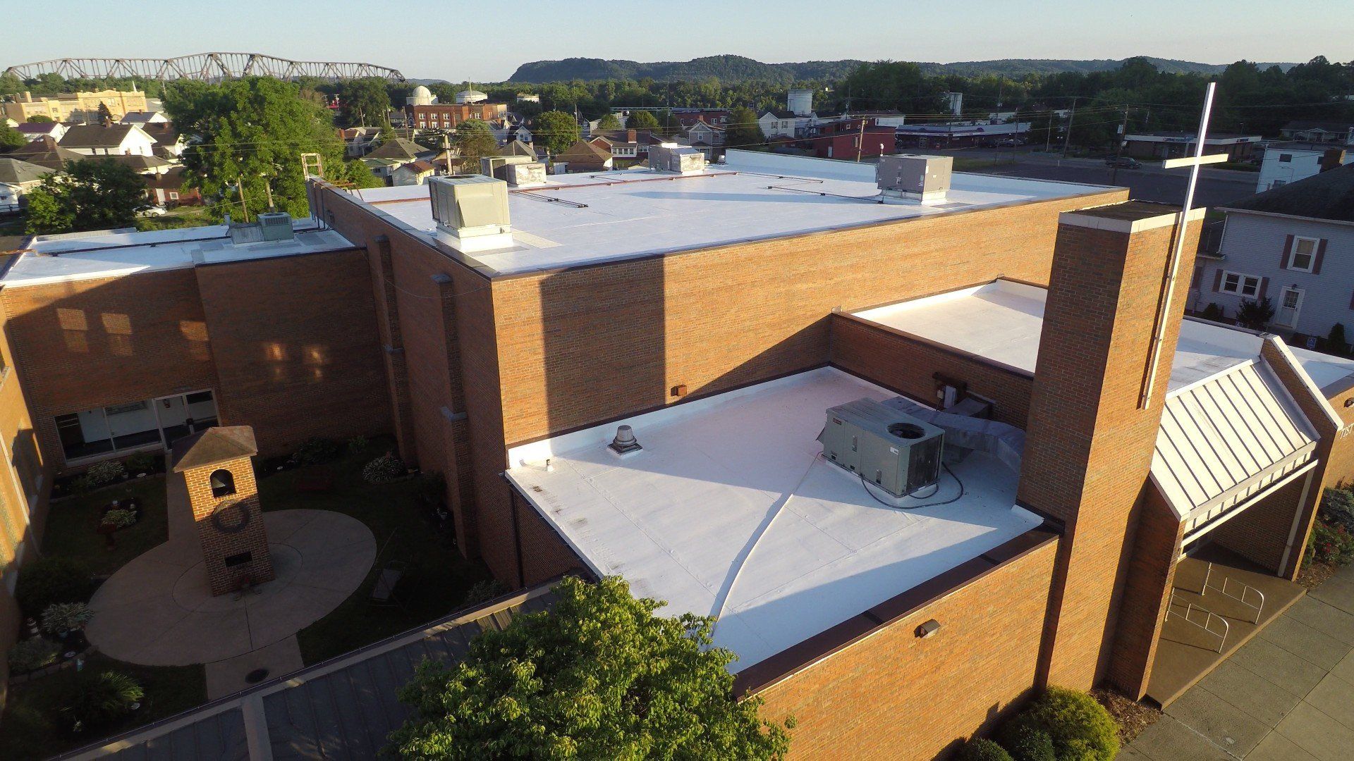 Brick church with white flat roofs, a cross, and surrounding buildings.