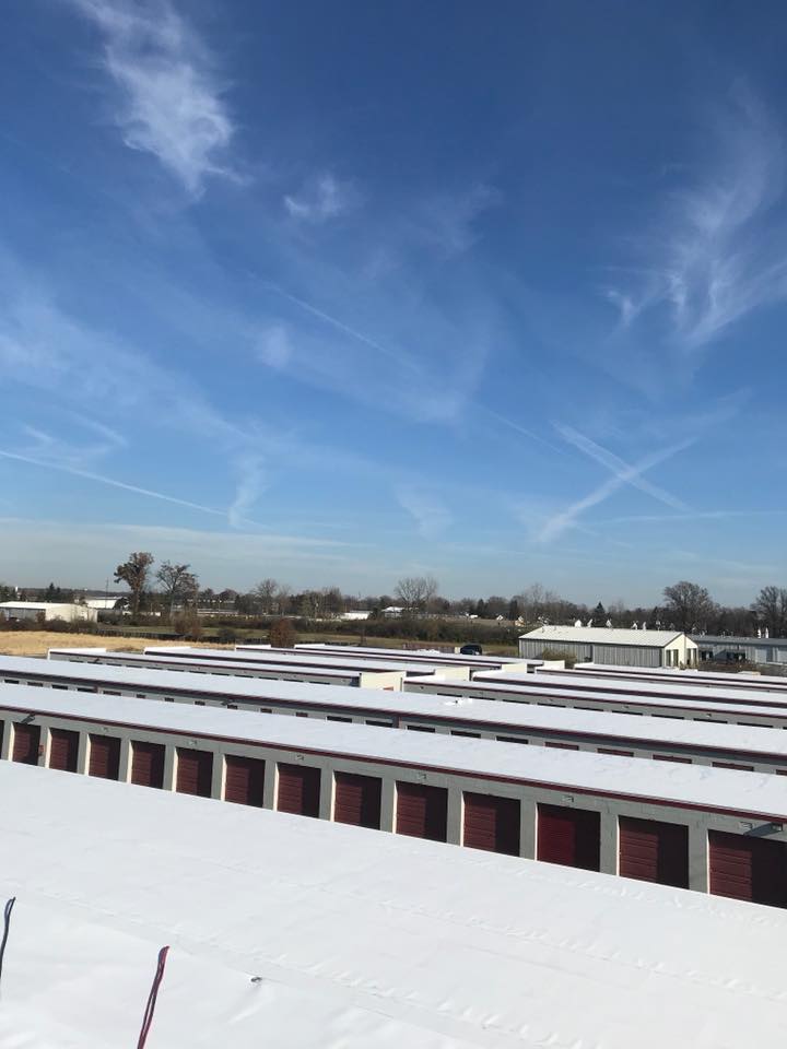 Rows of storage units covered in snow under a blue sky with contrails.