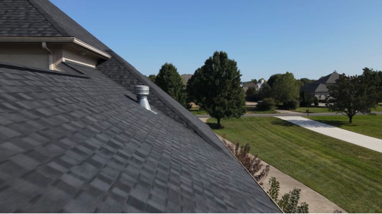 Dark gray shingle roof, metal vent, and a residential neighborhood in background.