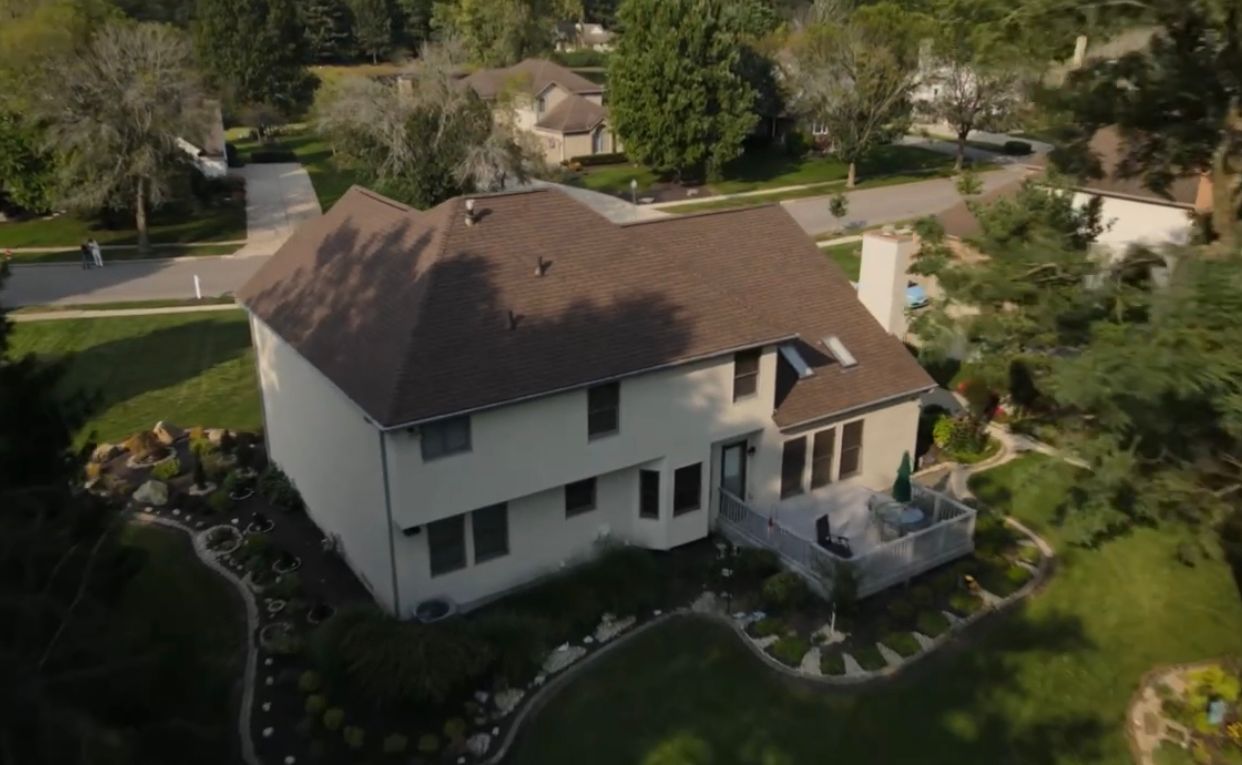 Two-story house with brown roof and beige siding, landscaped yard, sunny day.