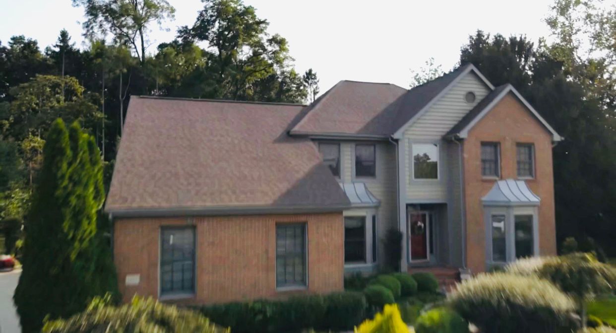 Two-story house with brick and siding, brown roof, and front yard landscaping under a blue sky.