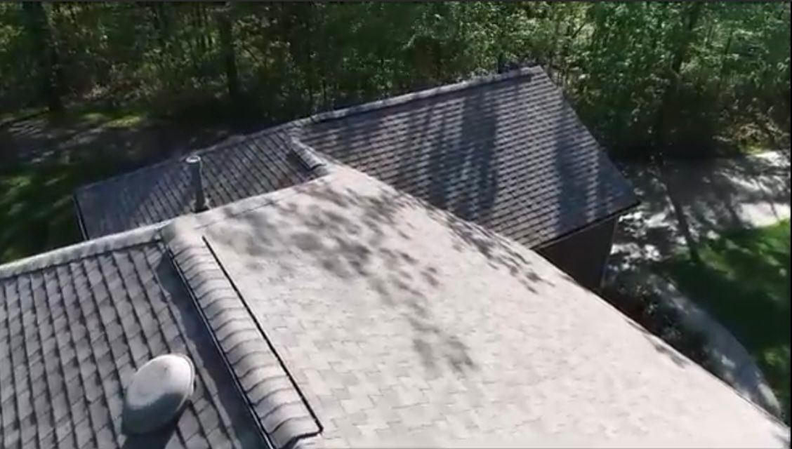Overhead view of a house roof with dark gray shingles and areas of darker discoloration.