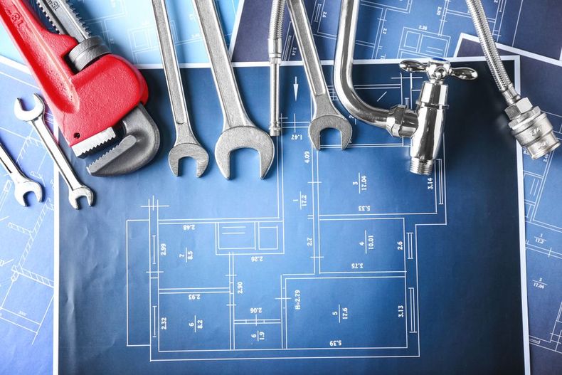 Plumbing tools on a blue blueprint plan with pipe fittings and a red wrench