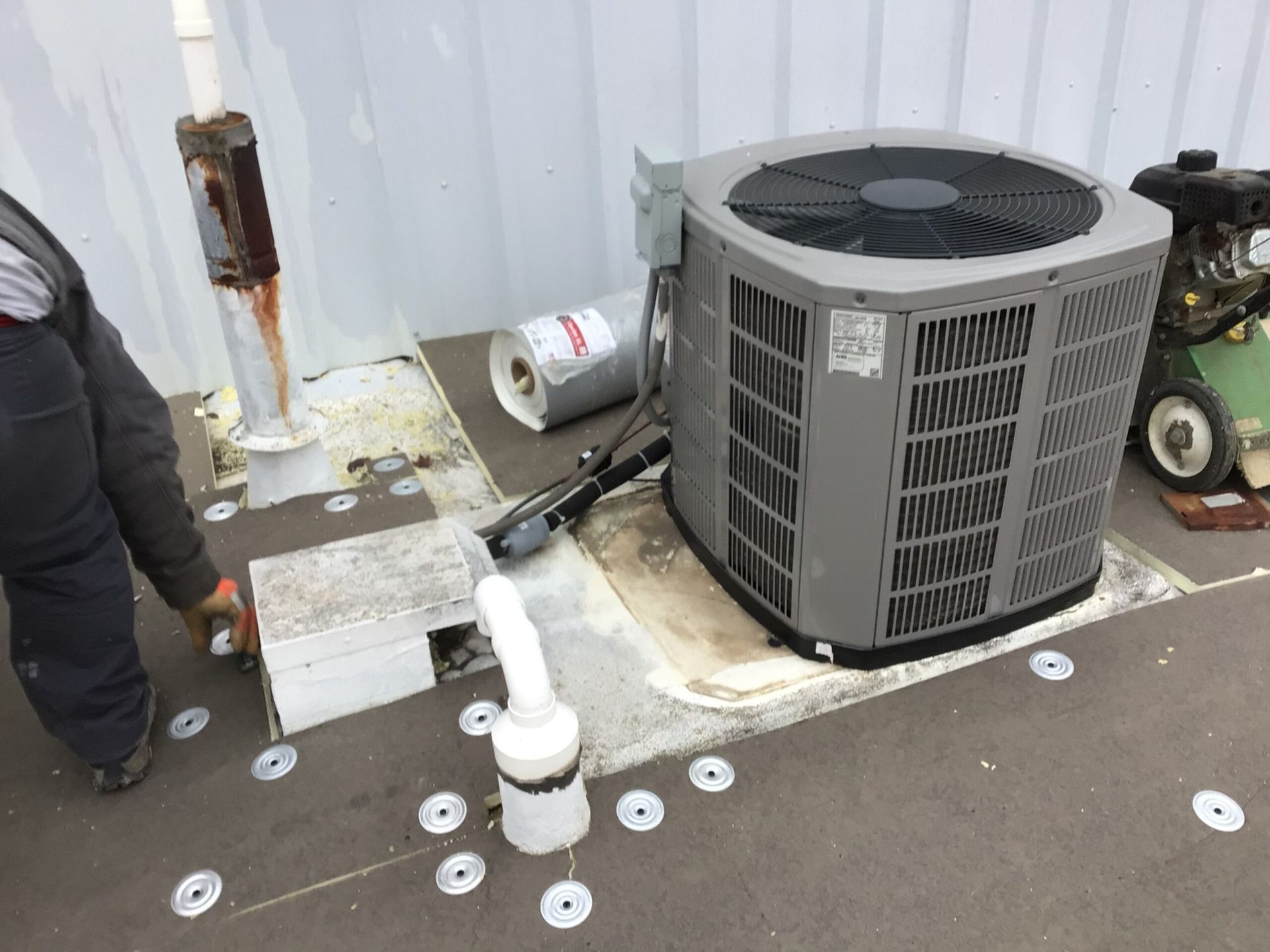HVAC unit on a roof with a person working on the piping near a white vent and rusty pipe.
