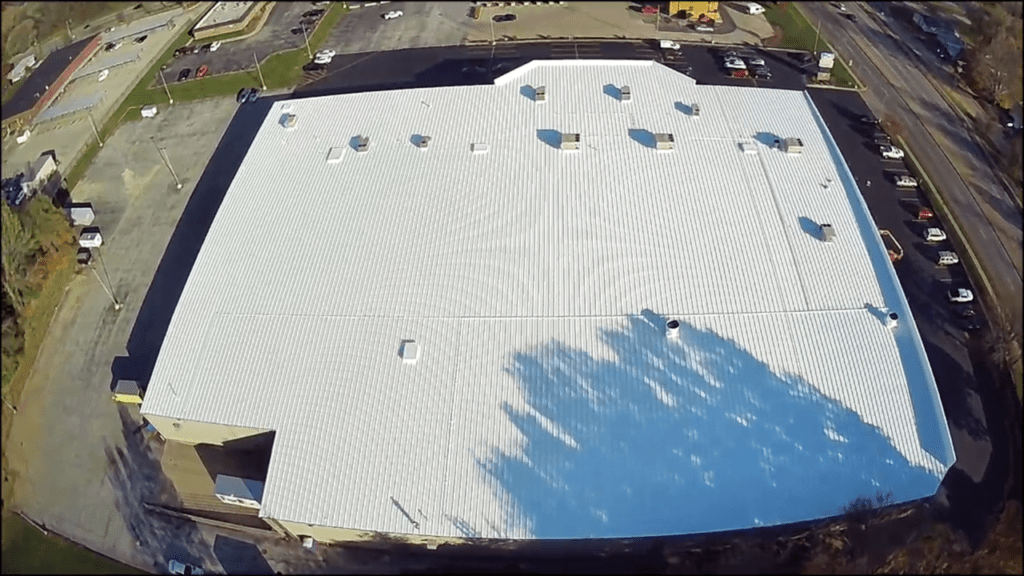 Aerial view of a large white building with a distinctive curved roof; sunny day.