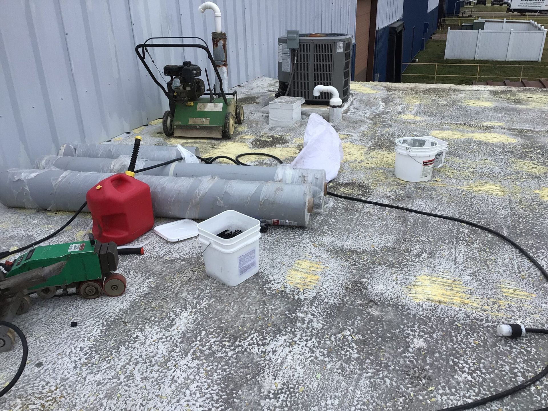 Exterior view with equipment on a concrete surface. Contains a lawn edger, gas can, air conditioner, and pipes.