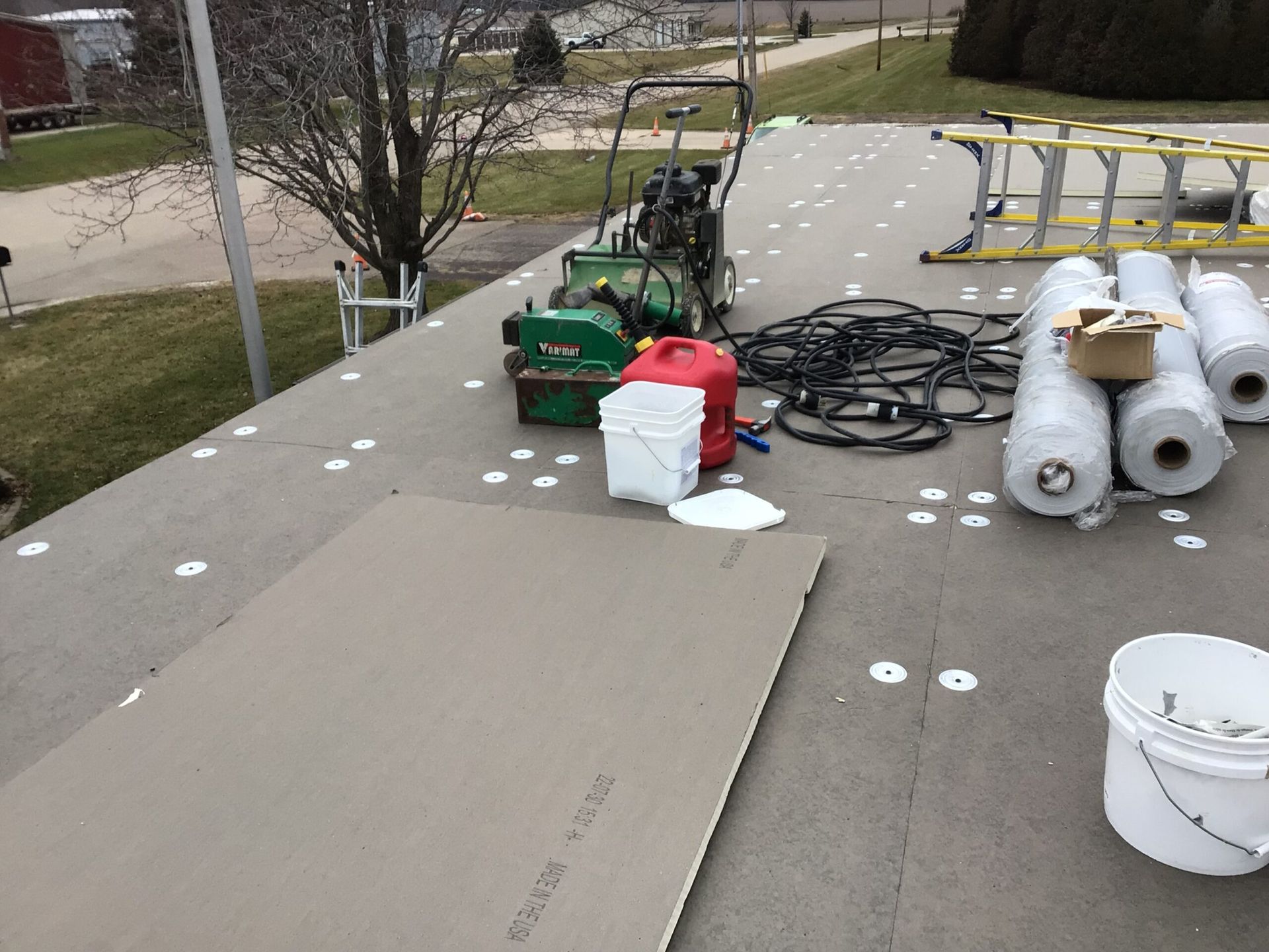 Roof construction site with equipment and materials, including rolled roofing and machinery.