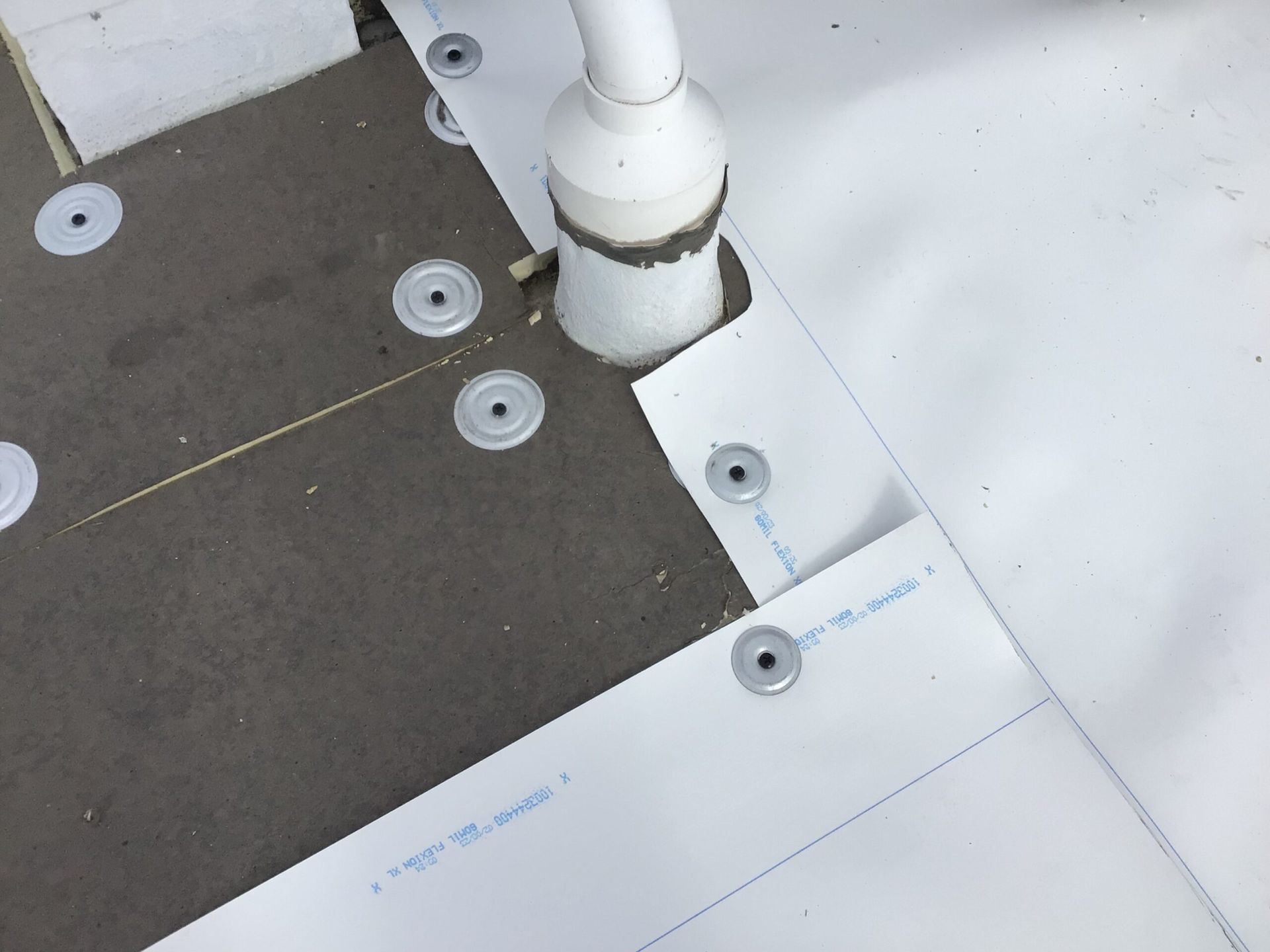 White roofing material being installed with washers around a pipe.