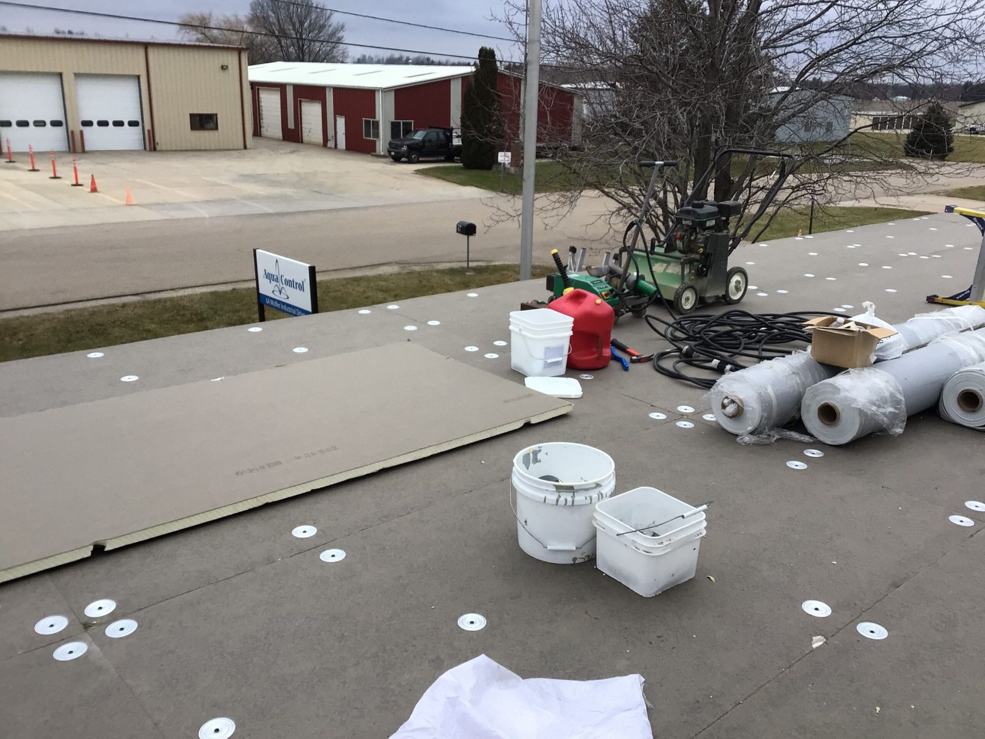 Roof with materials and equipment; building in the background. White discs, rolls, buckets, and a board are visible.