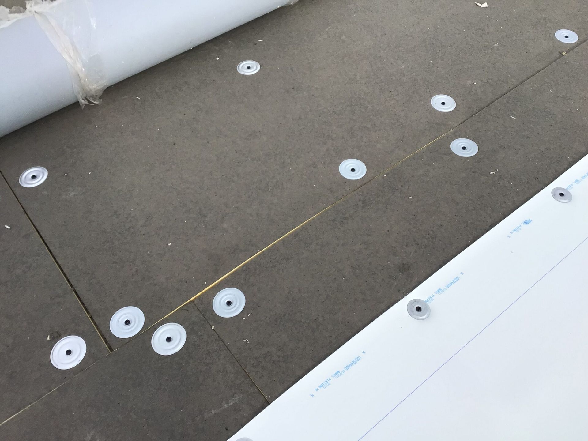 Dark gray roof insulation with white fasteners, partially covered by white material roll.
