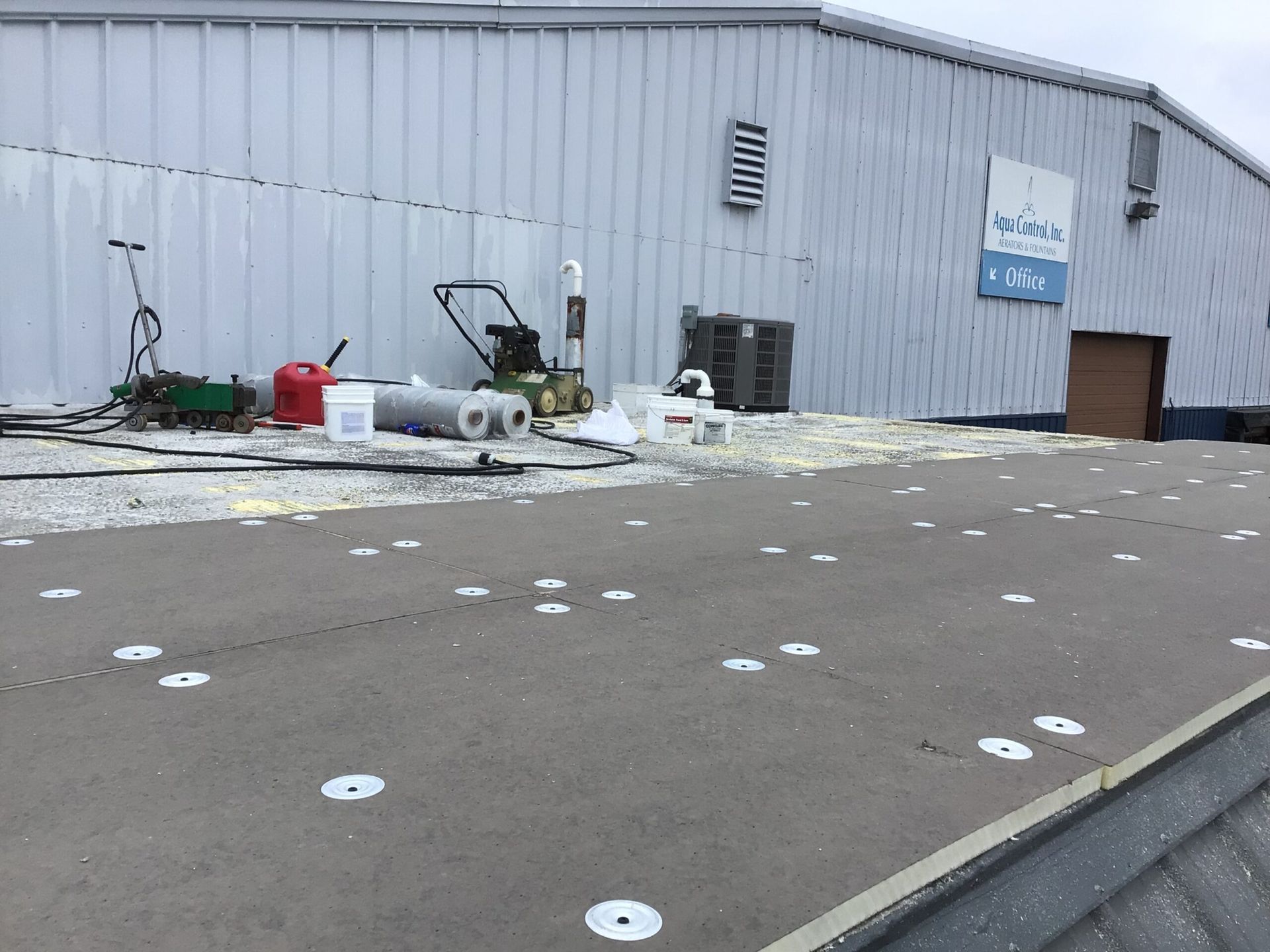 Flat commercial roof, with equipment and supplies staged along building wall.
