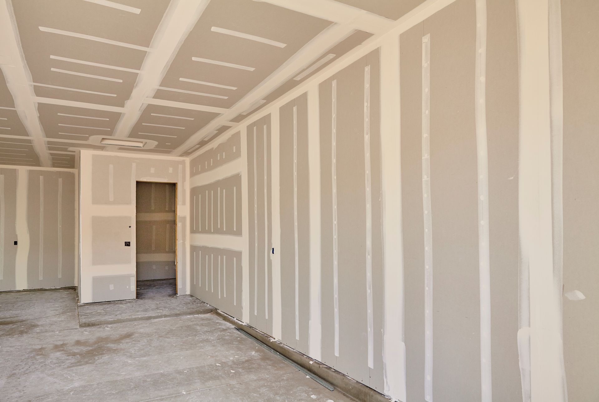 Unfinished drywall room with taped seams, open door, and bare concrete floor under construction