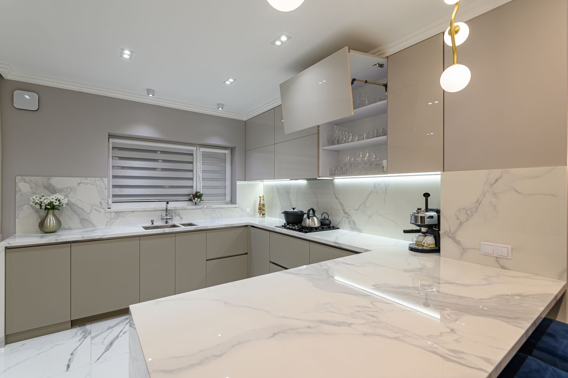 Modern beige-and-white kitchen with marble countertops, built-in cabinets, and pendant lights