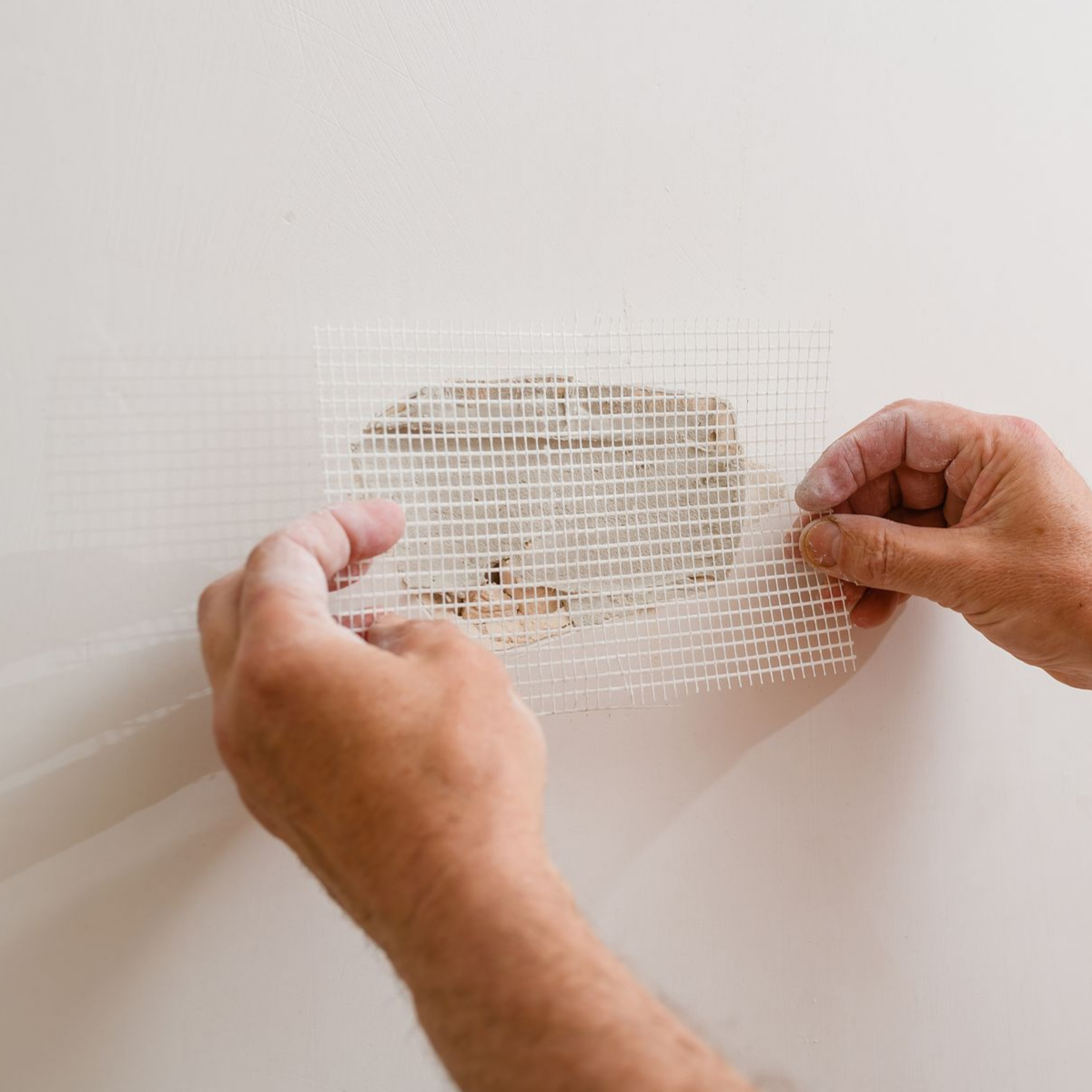 Hands applying drywall mesh tape over a wall patch hole. Hands applying drywall mesh tape over a wall patch hole.