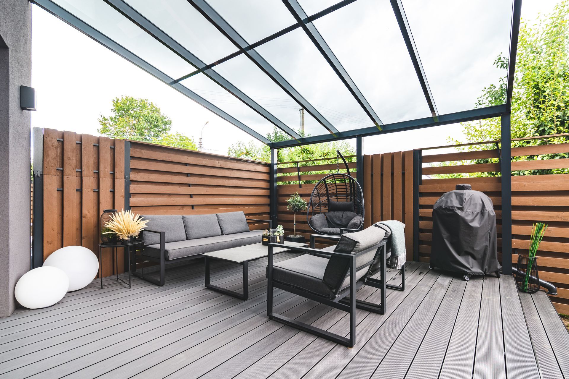 Modern patio with gray seating, wood slat fence, grill, and translucent roof panels