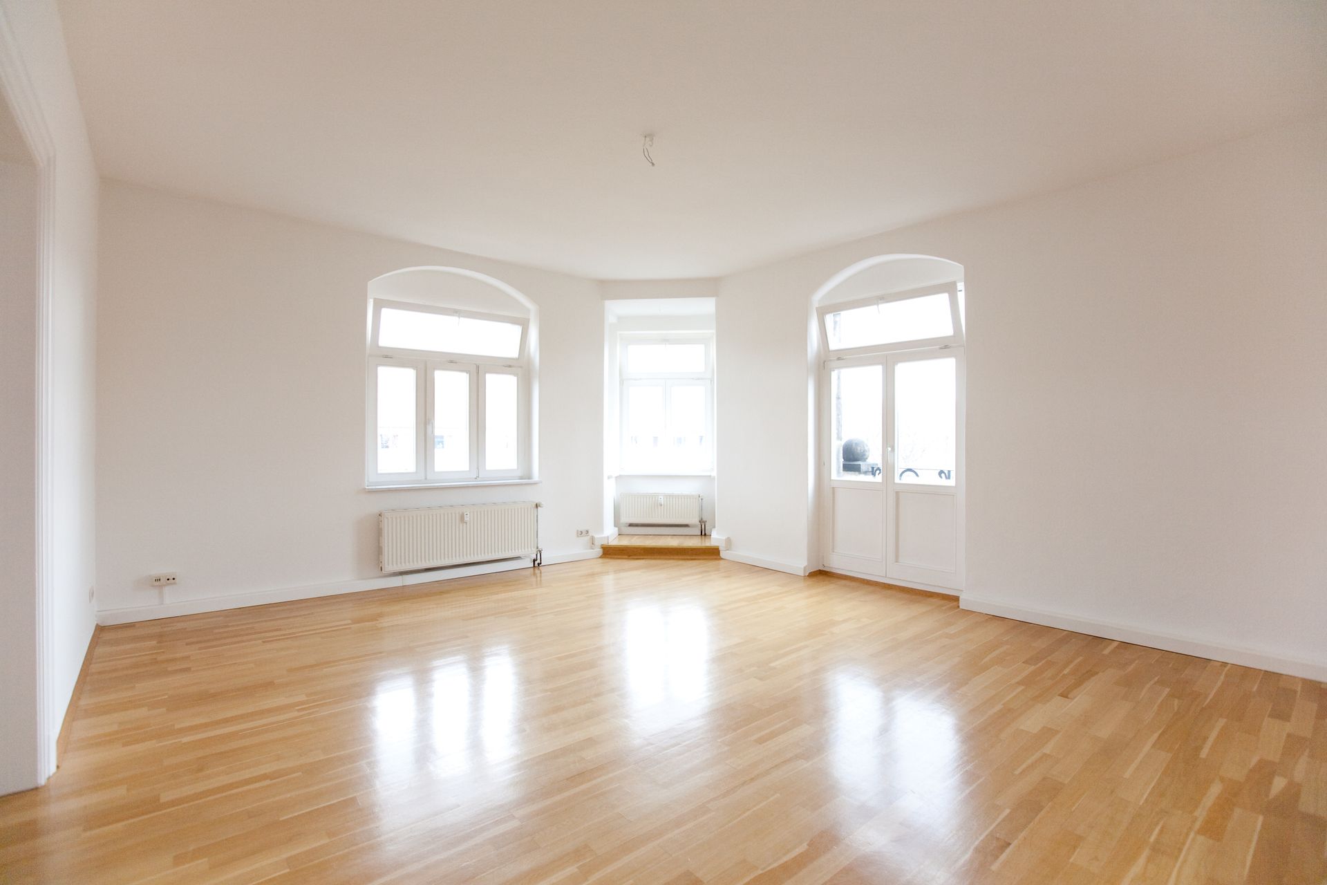 Bright empty room with hardwood floors, white walls, and three windows letting in natural light