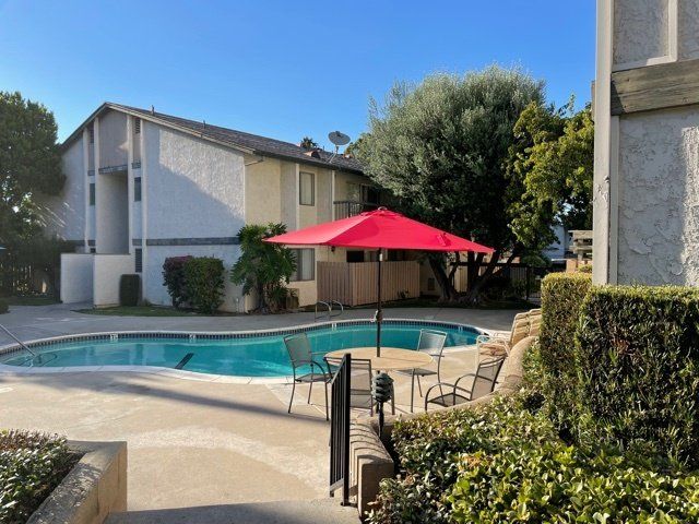 A swimming pool with a red umbrella in front of a building