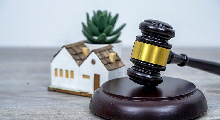 A wooden judge 's gavel is sitting on a wooden table next to a model house.