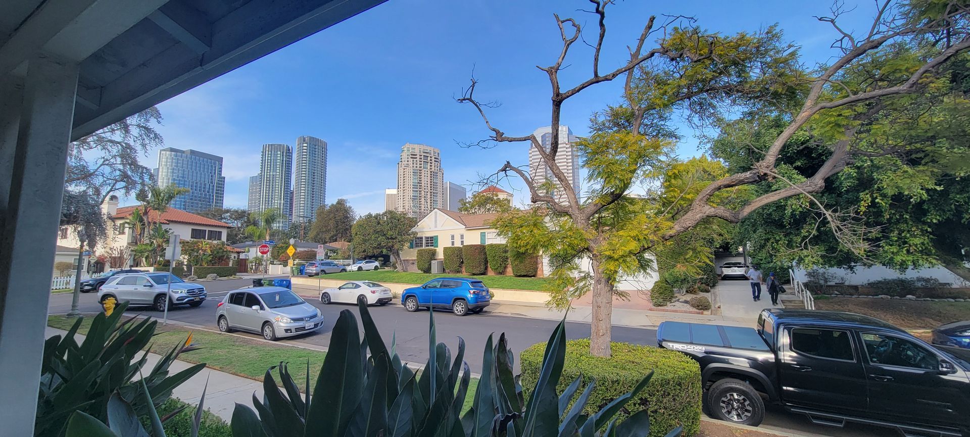 A view of a city street from a porch with cars parked on the side of the road.