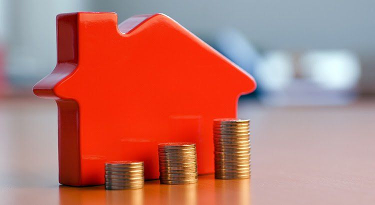 A red house sitting on top of a table next to stacks of coins.