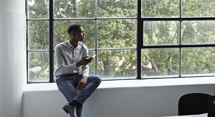 A man is sitting on a window sill using a cell phone.