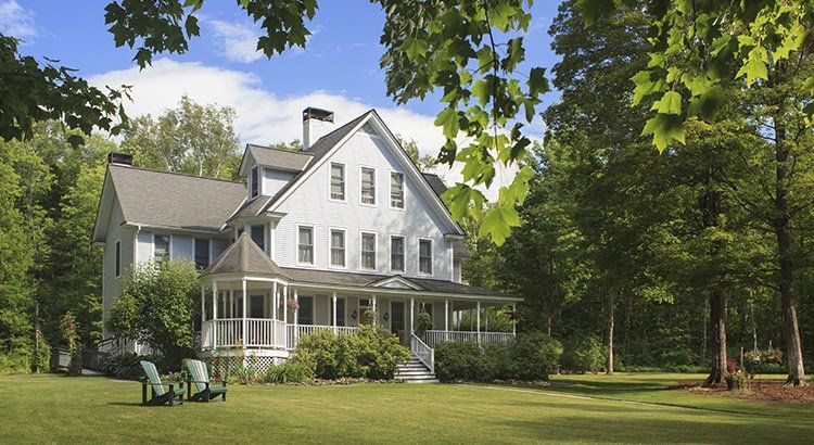 A large white house with a porch and chairs in front of it